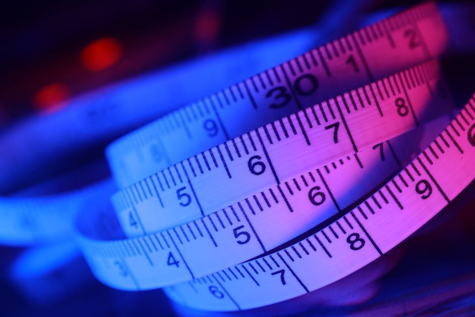 A close-up image of a flexible measuring tape with white background and black markings, curled and layered to show various measurement points from 4 to 9 inches. The tape features a gradient color sch