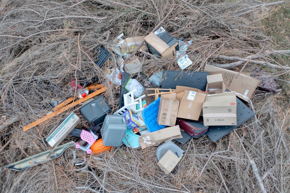A large open area covered with scattered waste materials, including discarded tires, plastic bags, cardboard boxes, and various debris. The rubbish is piled unevenly across the ground, creating a clut